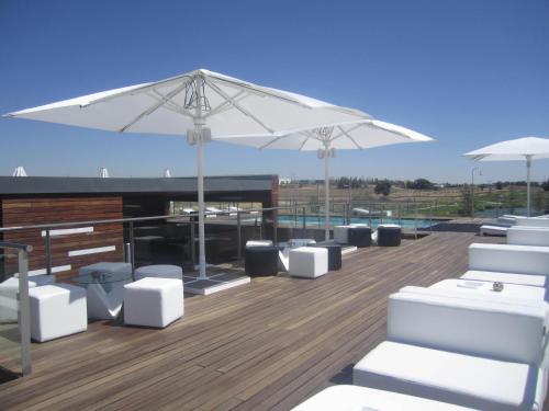 a patio with white chairs and umbrellas on a deck at Sercotel El Encin Golf in Alcalá de Henares