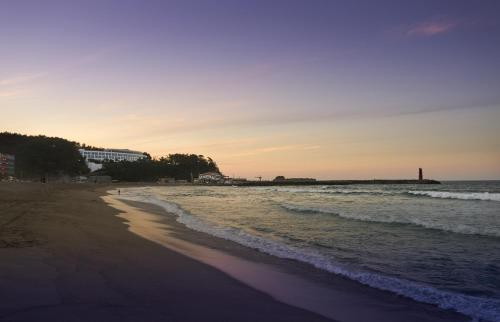a beach with the ocean and a lighthouse in the distance at Naksan Beach Hotel in Yangyang