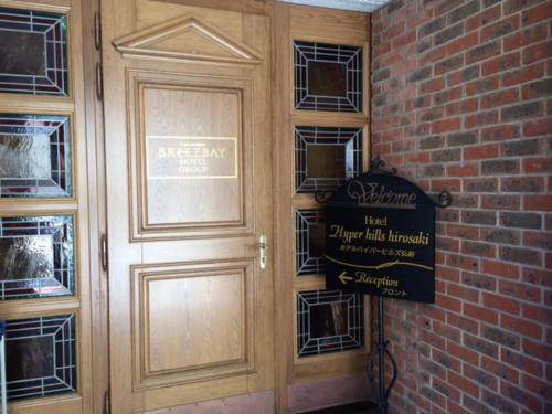 a wooden door with a sign next to a brick wall at Hotel Hyper Hills Hirosaki in Hirosaki