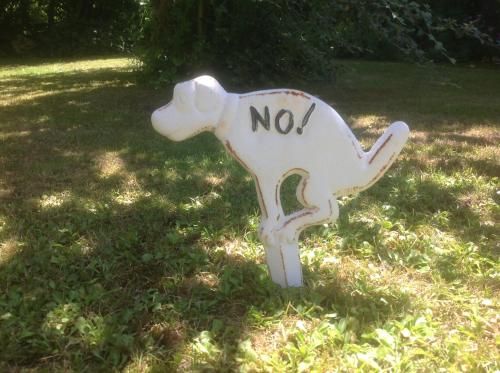a white dog sign sitting in the grass at Au Fond du Jardin Maison d'hôtes in Saint-Saëns