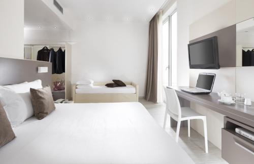 a white bedroom with a bed and a desk with a laptop at Hotel Cube in Ravenna