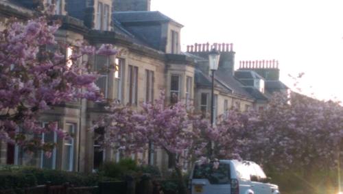 a van parked in front of a building with purple trees at Lochinver Guesthouse in Ayr