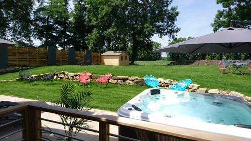a hot tub on a deck with chairs and an umbrella at Le Moulin d'Oscar & Spa - Mulhouse Nord in Baldersheim