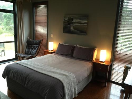 a bedroom with a bed and two lamps and a chair at Piha Beachstay Accommodation in Piha