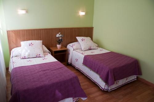 two beds in a small room with purple sheets at Hostal Restaurante La Cepa in Cariño
