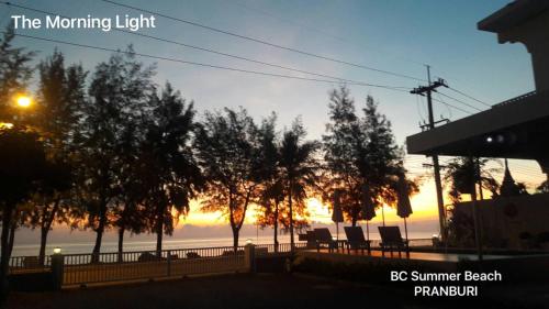 a sunset over a fence with chairs and trees at BC Summer Beach in Pran Buri
