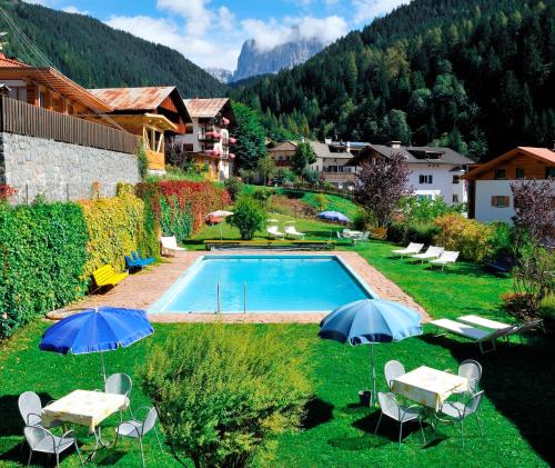 a swimming pool with tables and umbrellas in a yard at Hotel Central in Nova Levante