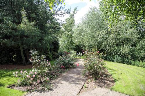 a garden with flowers and trees and a sidewalk at Quorn Country Hotel Leicester in Loughborough
