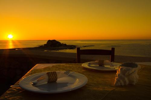 a table with plates and utensils on it with the sunset at Al Mare Villas in Kiotari