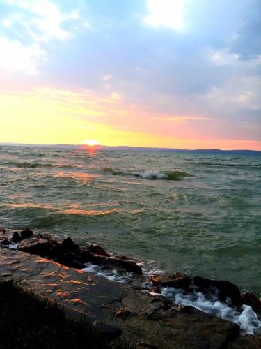 a sunset over the ocean with rocks in the water at Princess Luxus Apartman in Siófok