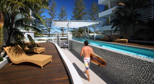 a man carrying a surfboard next to a swimming pool at Rumba Beach Resort in Caloundra