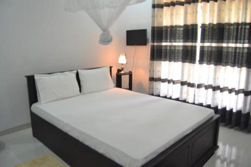 a bedroom with a bed with white sheets and a window at Lovely lodge & Hostel in Sigiriya