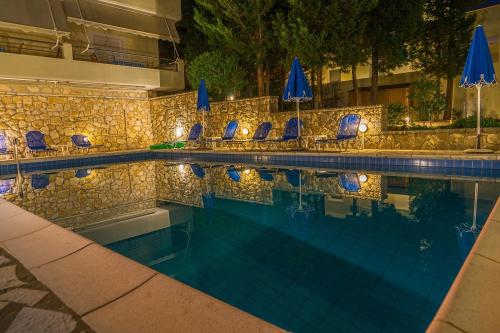 a swimming pool with chairs and blue umbrellas at Geni Garden Apartments in Yenion