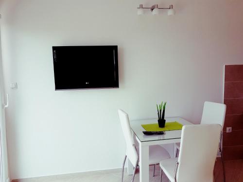 uma mesa branca com cadeiras brancas e uma televisão na parede em Apartman Milovic em Tivat