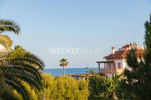 a house on the beach with palm trees and the ocean at Villa Sitges Tupinetti Beach at 1 min walk Amaizing Garden and View Center Sitges 5 minutes walk in Sitges