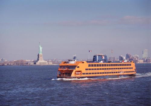 a large yellow boat in the water with the statue of liberty at voco Times Square South New York by IHG in New York
