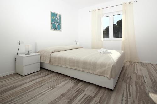 a white bedroom with a bed and a window at Apartments Močići in Močići