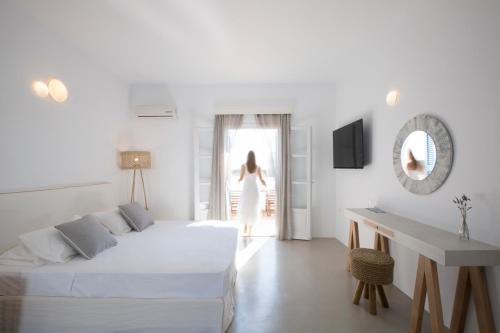 a woman walking into a white room with a bed at Kouros Village in Antiparos Town