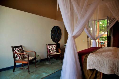 a bedroom with a bed and two chairs and a window at Jardim dos Aloés, Unique B&B - Casa de Charme in Ilha de Moçambique