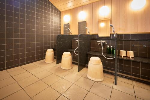 a bathroom with three urinals and three sinks and a shower at Hotel Kan Raku Honjo Waseda Ekimae in Honjo