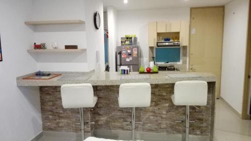 uma cozinha com um balcão com quatro cadeiras brancas em Apartamento con salida al Mar em Santa Marta