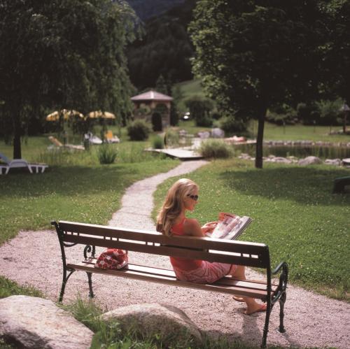 a woman sitting on a park bench reading a magazine at Naturhotel MOLIN in San Giovanni in Val Aurina