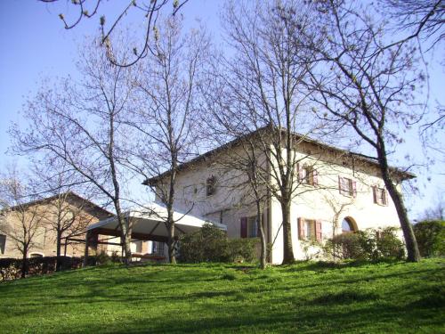 a white house on a grassy hill with trees at Agriturismo Montevecchio Isolani in Monte San Pietro