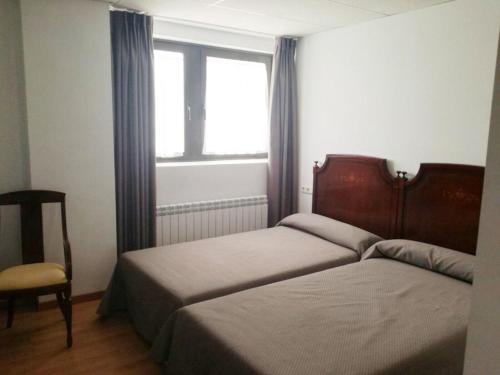 1 dormitorio con 2 camas, ventana y silla en Pension La Espiga en Pamplona