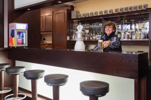 a woman is standing behind a bar with stools at Best Western Hotel Augusta in Augsburg
