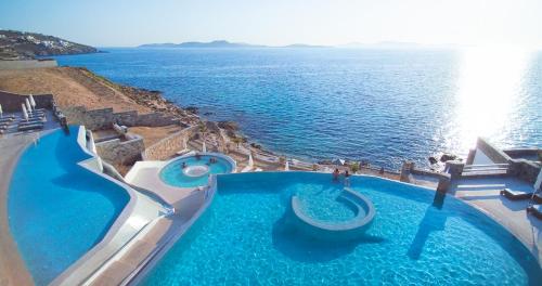 
a beach with a pool and chairs and a blue ocean at Anax Resort and Spa in Agios Ioannis Mykonos
