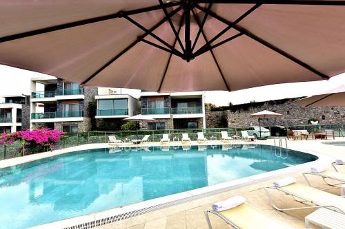 a large swimming pool with an umbrella and chairs at Degirmenburnu Residence in Bodrum City