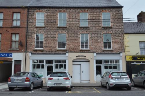 two cars parked in a parking lot in front of a brick building at Blessings Studio Apartments in Cootehill
