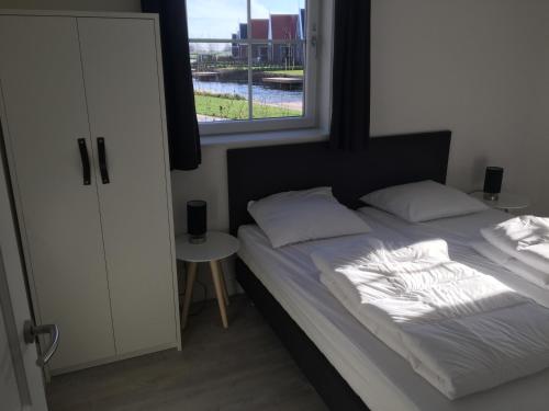 a bed with white sheets and pillows and a window at Luxurious Water Villa in Uitdam
