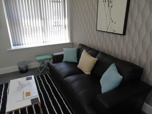 a living room with a black leather couch and a table at Jeffersons Hotel & Serviced Apartments - The Steel Works in Barrow in Furness
