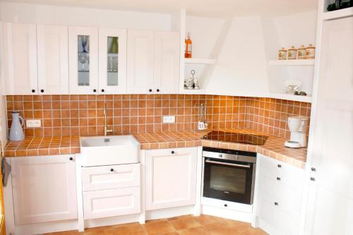 a kitchen with white cabinets and orange tile on the wall at Maison du Chat in Bargemon