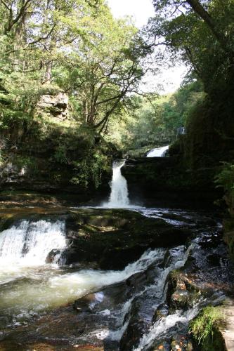 a river with a waterfall in a forest at Nant Ddu Lodge Hotel & Spa in Merthyr Tydfil