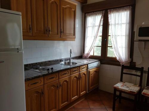 cocina con armarios de madera, fregadero y nevera en Casa Rural Oihan - Eder en Espinal-Auzperri