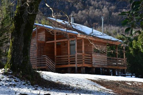 a log cabin in the snow next to a tree at Cabañas en Alojamientos Techo Azul in Malalcahuello