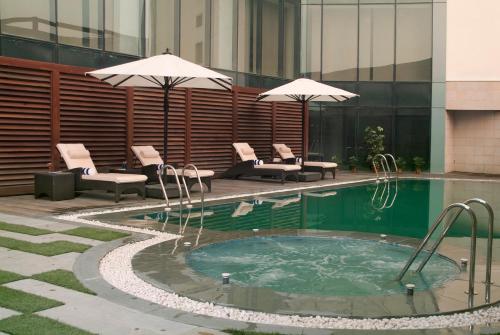 einen Pool mit Stühlen und Sonnenschirmen neben einem Gebäude in der Unterkunft Savoy Suites Greater Noida in Greater Noida