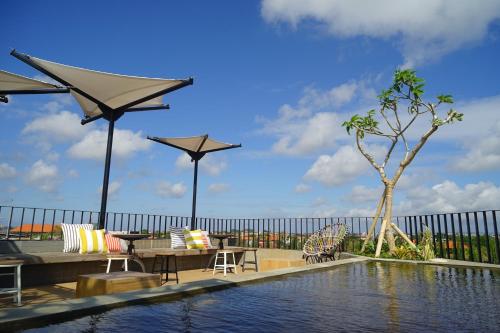 a swimming pool with tables and chairs and umbrellas at Borough Capsule Hostel Bali in Legian