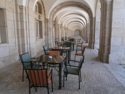 Una fila de mesas y sillas en un pasillo vacío. en Hospedería Santa Cruz, en San Lorenzo de El Escorial