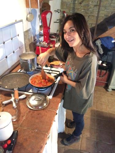 a woman standing in a kitchen preparing food in a pan at b&b LATORDICELLA in Castel del Rio