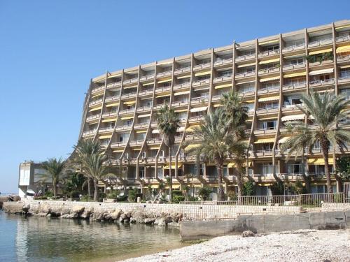 a large building with palm trees in front of a body of water at St Paul Resort in Safra