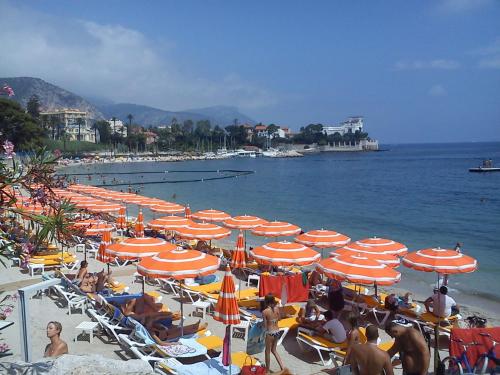 a beach with many umbrellas and people on the beach at Résidence Carlton - Rénovée avec Piscine in Beaulieu-sur-Mer