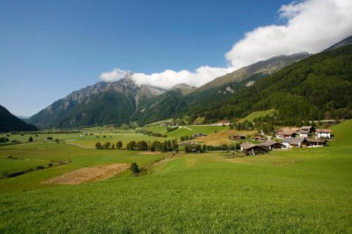 a green field with houses and mountains in the background at Hotel Kranebitt in Val di Vizze