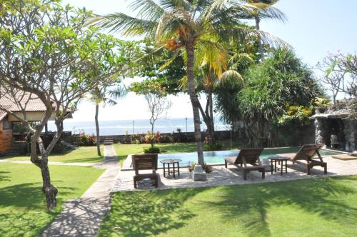 a pool with benches and palm trees and the ocean at Pondok Bali Sea View Bungalow in Lovina