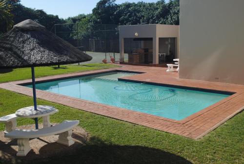a swimming pool with a umbrella and a chair and a table at 5 Key Largo in Amanzimtoti