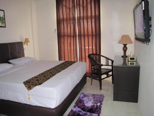 a bedroom with a bed and a chair and a television at Hotel Mitra Garden in Pangkal Pinang