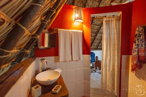 a bathroom with red walls and a white sink at Pousada Capitù in Imbassai
