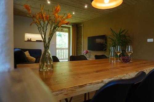a wooden table with a vase of flowers and wine glasses at ecoHouse FURLAN - Apartment PINJA in Kobarid